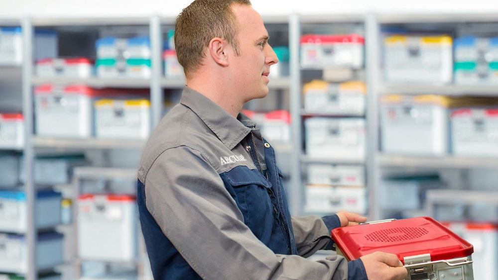 A B. Braun technical service maintenance worker is handing over a box containing replacement parts for medical devices.