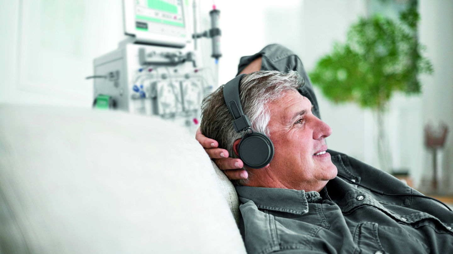 Hombre tumbado en una cama con la parte superior del cuerpo elevada por la almohada o el respaldo. Se puede ver un monitor de diálisis en segundo plano.