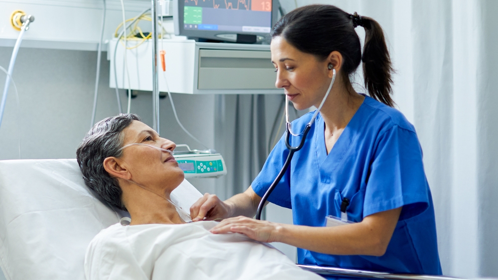 A patient in a hospital bed is examined by a doctor with a stethoscope