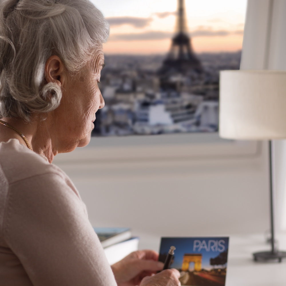 An elderly woman at her desk, enjoying a scenic view of the Eiffel Tower in the background.
