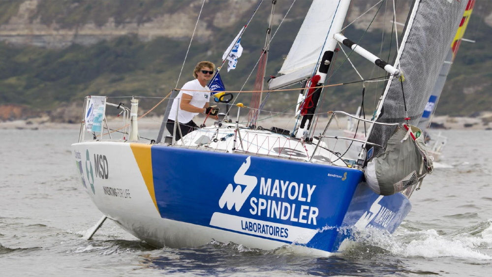 Een man zeilt op een jacht door snel bewegend water, met golven die tegen de romp spatten