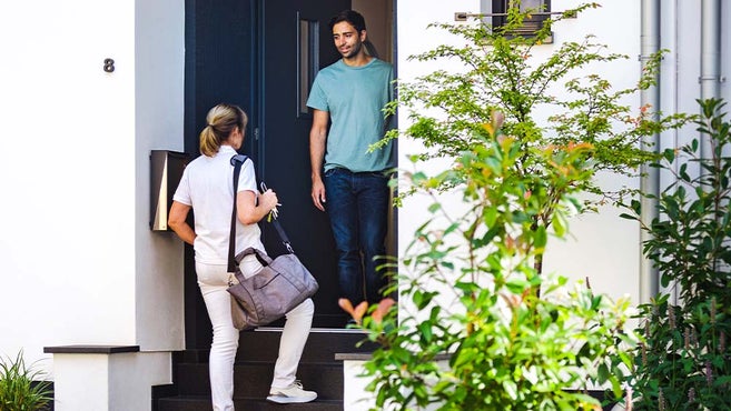 female nurse and male patient standing in the front door of patient's home