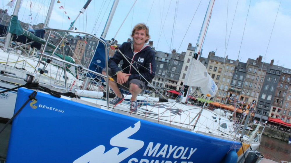 Ein Mann sitzt mit einem Lächeln auf einer Yacht, im Hintergrund ein Hafen