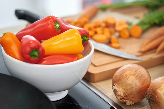 Ingezoomde afbeelding van een paprika, uien en een wortel die op een tafel liggen, met een mes ernaast