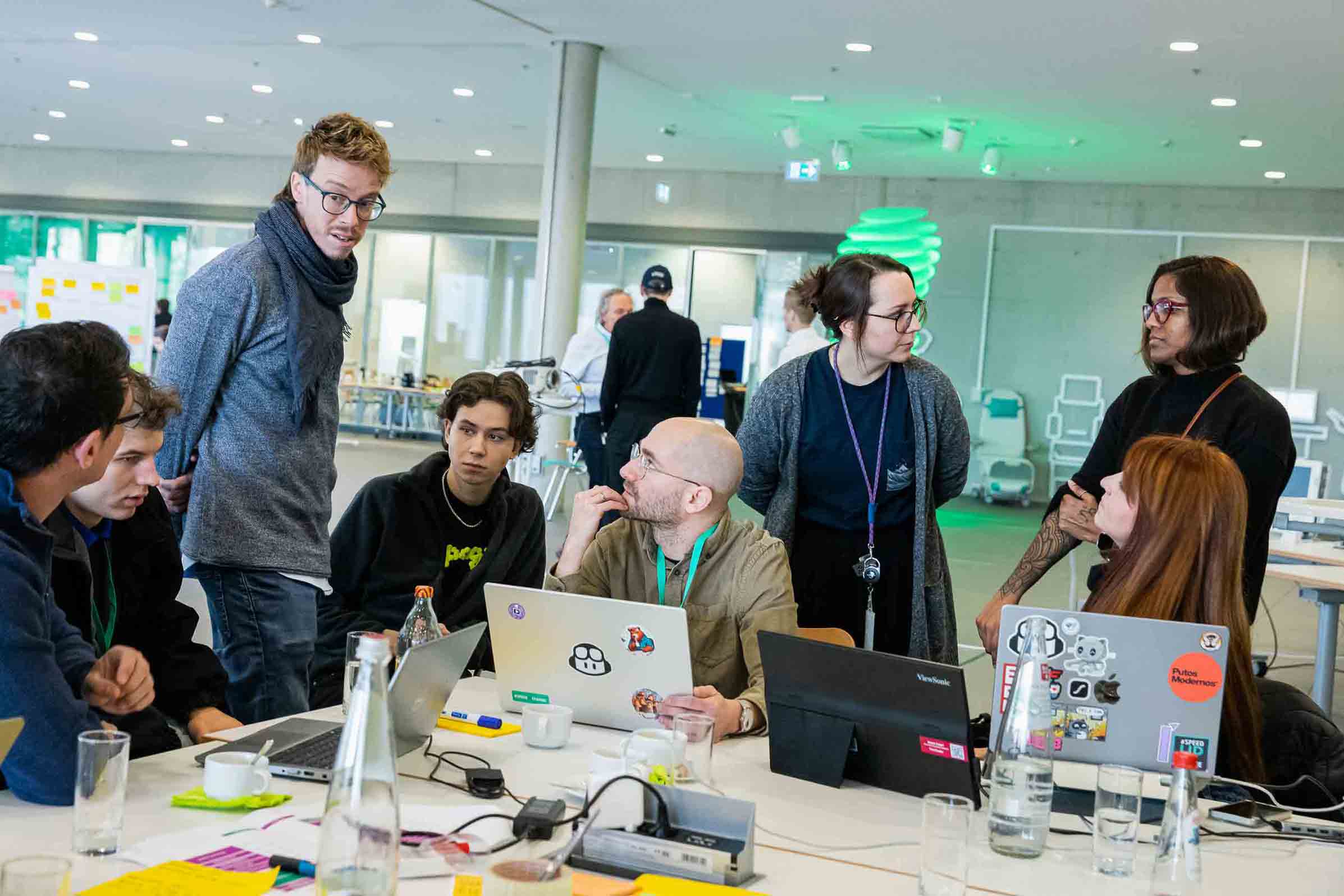 Grupo colaborando alrededor de una mesa con portátiles y notas en una oficina abierta.