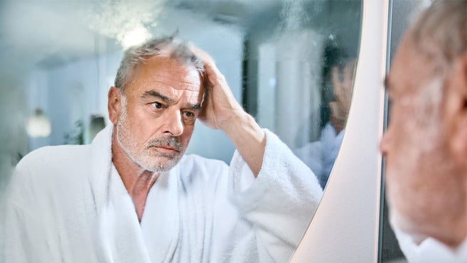 eldre mann i badekåpe ser tankefullt inn i et duggete badespeil
