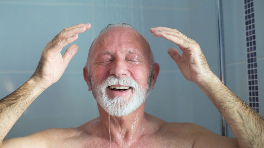 Un anziano in piedi sotto la doccia, sorridendo con l'acqua che scorre