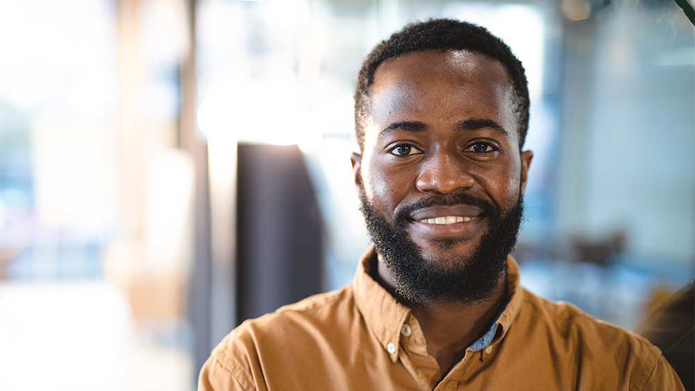 Nærbillede af en mand, der kigger ind i kameraet, smiler og har en orange skjorte på i lyse omgivelser. 