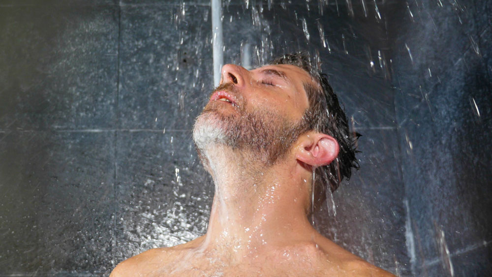A man is standing in the shower with the water running