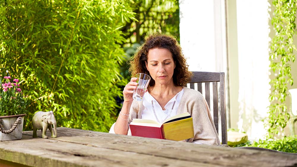 Una mujer sentada en una silla leyendo un libro y sosteniendo un vaso en la mano