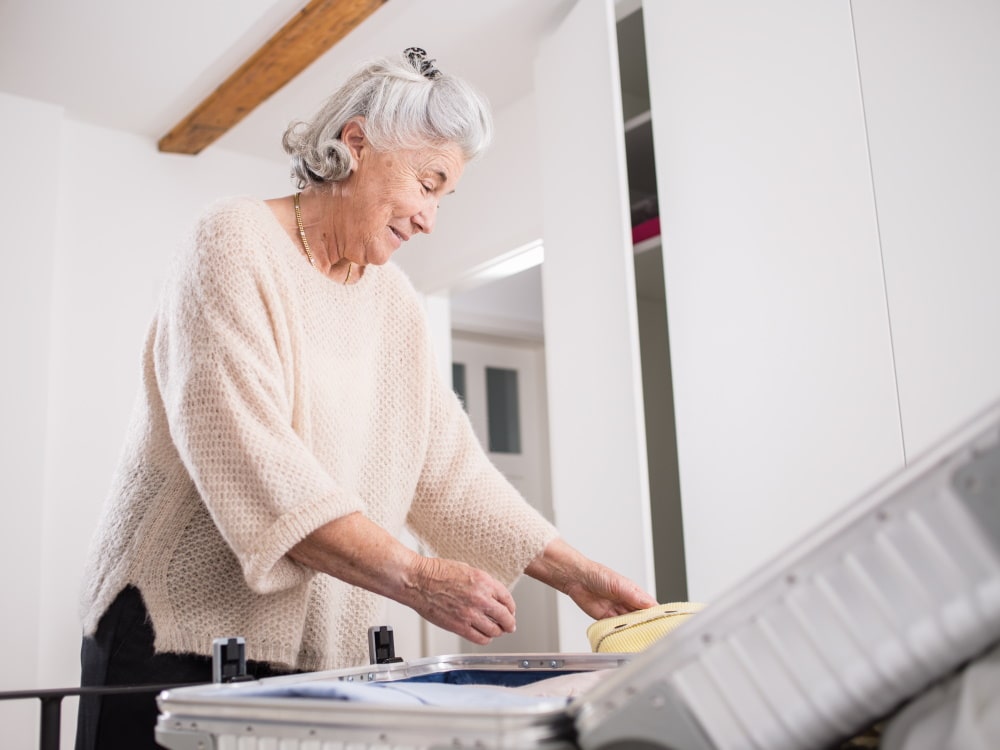 Iäkäs nainen pakkaa matkalaukkuansa ja hymyilee