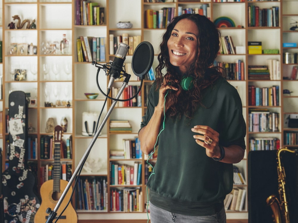 Femme devant un microphone dans un studio d’enregistrement à domicile, avec des instruments de musique en arrière-plan