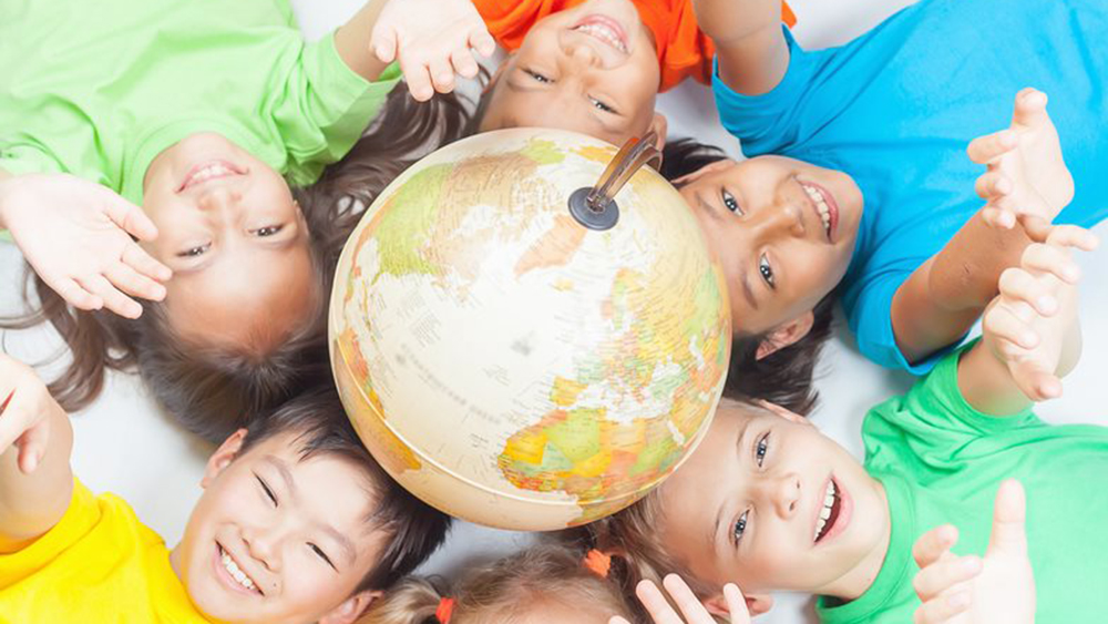 Bambini sorridenti sdraiati intorno a un globo sul pavimento mentre allungano le braccia verso l'alto.
