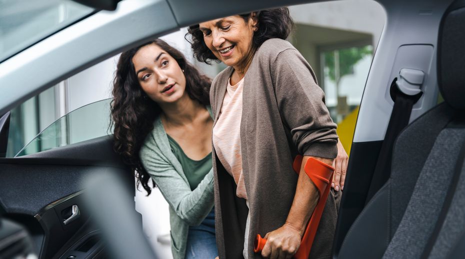 患者が椅子を使い、別の人物が車に乗り込むのを手伝っている。