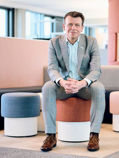 ミヒャエル・ラウク博士は、現代のオフィスで赤いファブリックのスツールに座り、笑顔で手をつないでいます。 