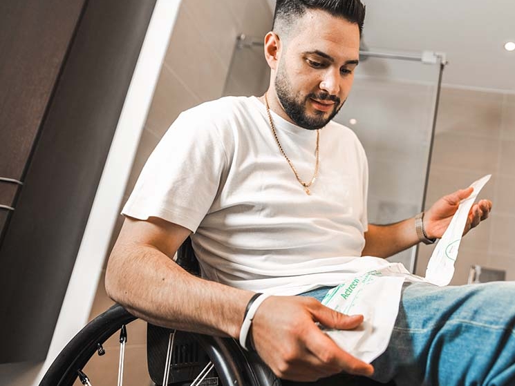 Muž na invalidnom vozíku, v pozadí kúpeľňa, v ruke drží katéter