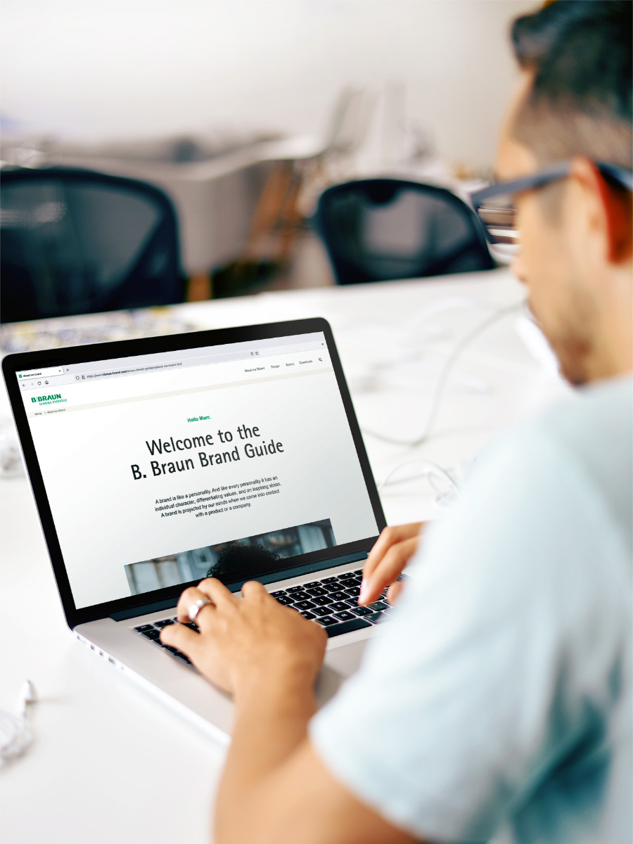 Một người đàn ông mặc áo sơ mi màu xanh nhạt đang vận hành máy tính xách tay với trang web B. Braun mở.